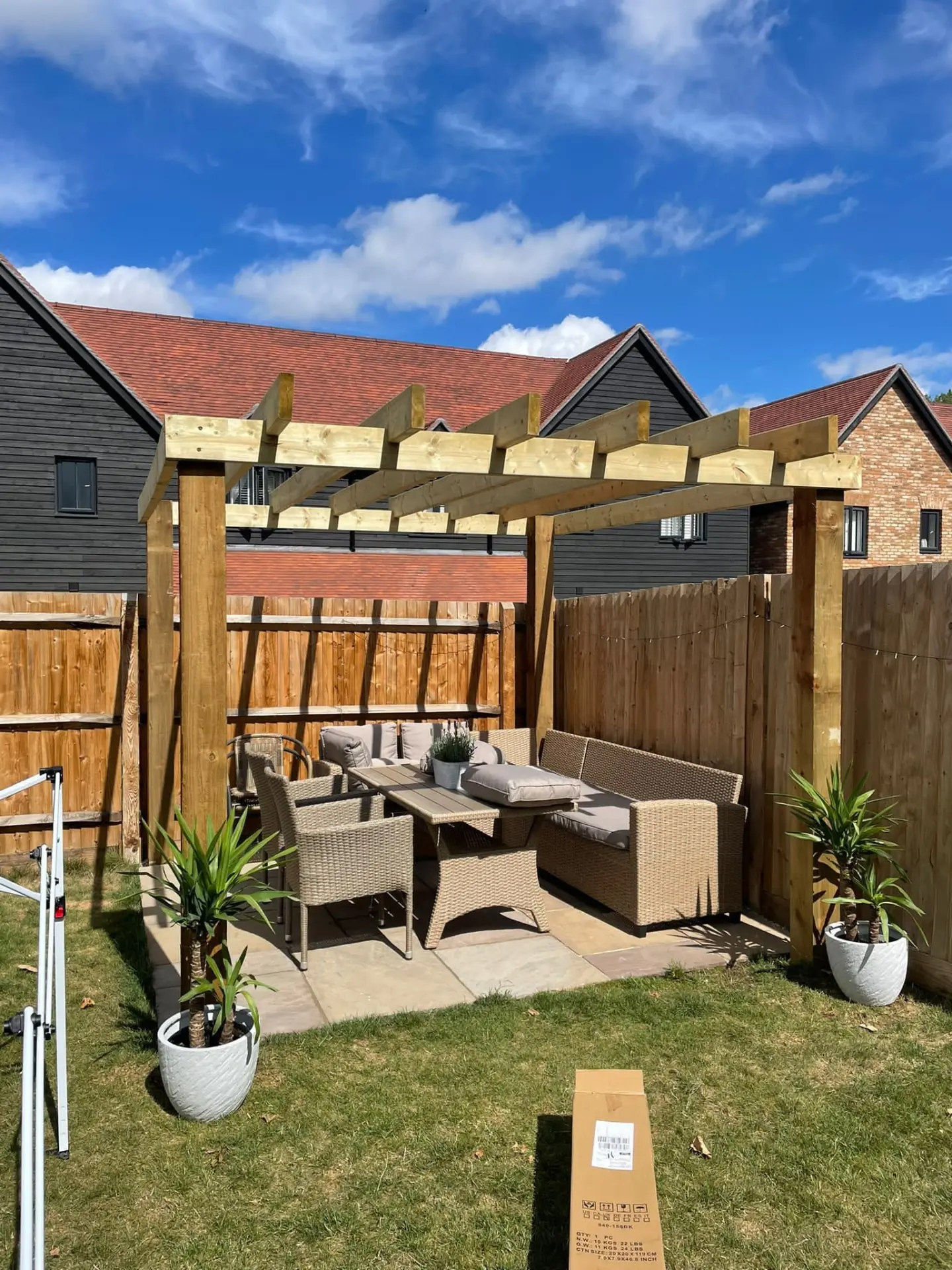 Newly built timber pergola over a sandstone patio with rattan corner seating in an Essex garden