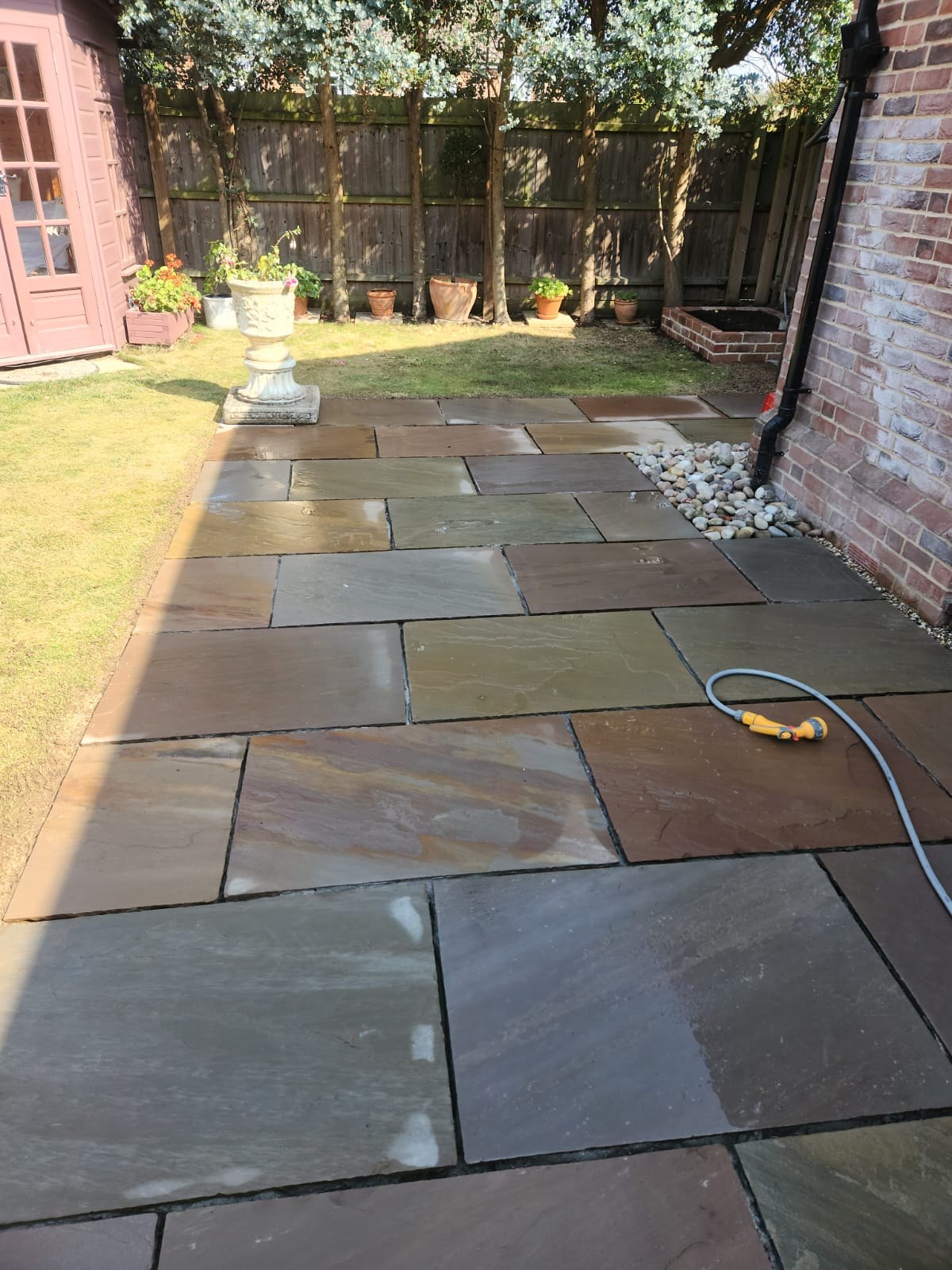 Riven sandstone patio wrapping around a brick house with pebble drainage margin
