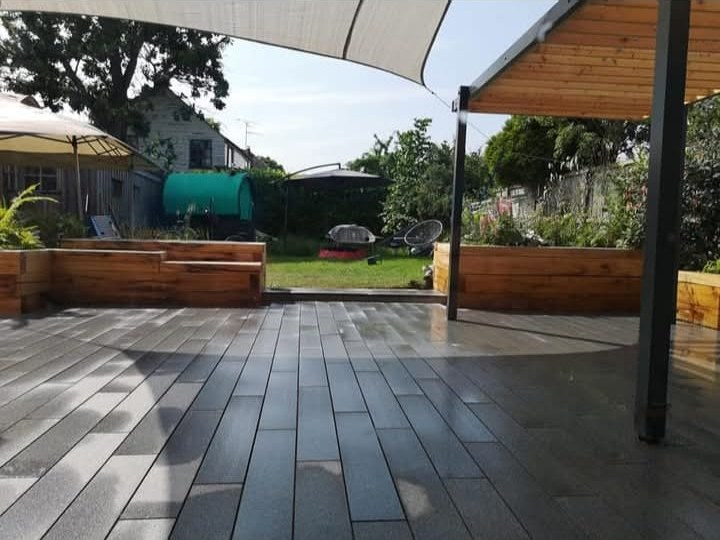 Grey composite decking with timber raised beds and a shade sail over the seating area