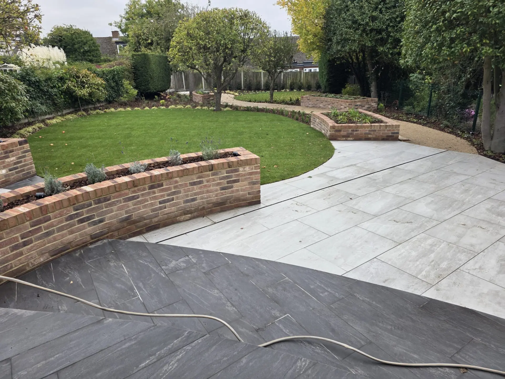 Freshly laid circular lawn framed by curved brick raised beds and grey porcelain paving