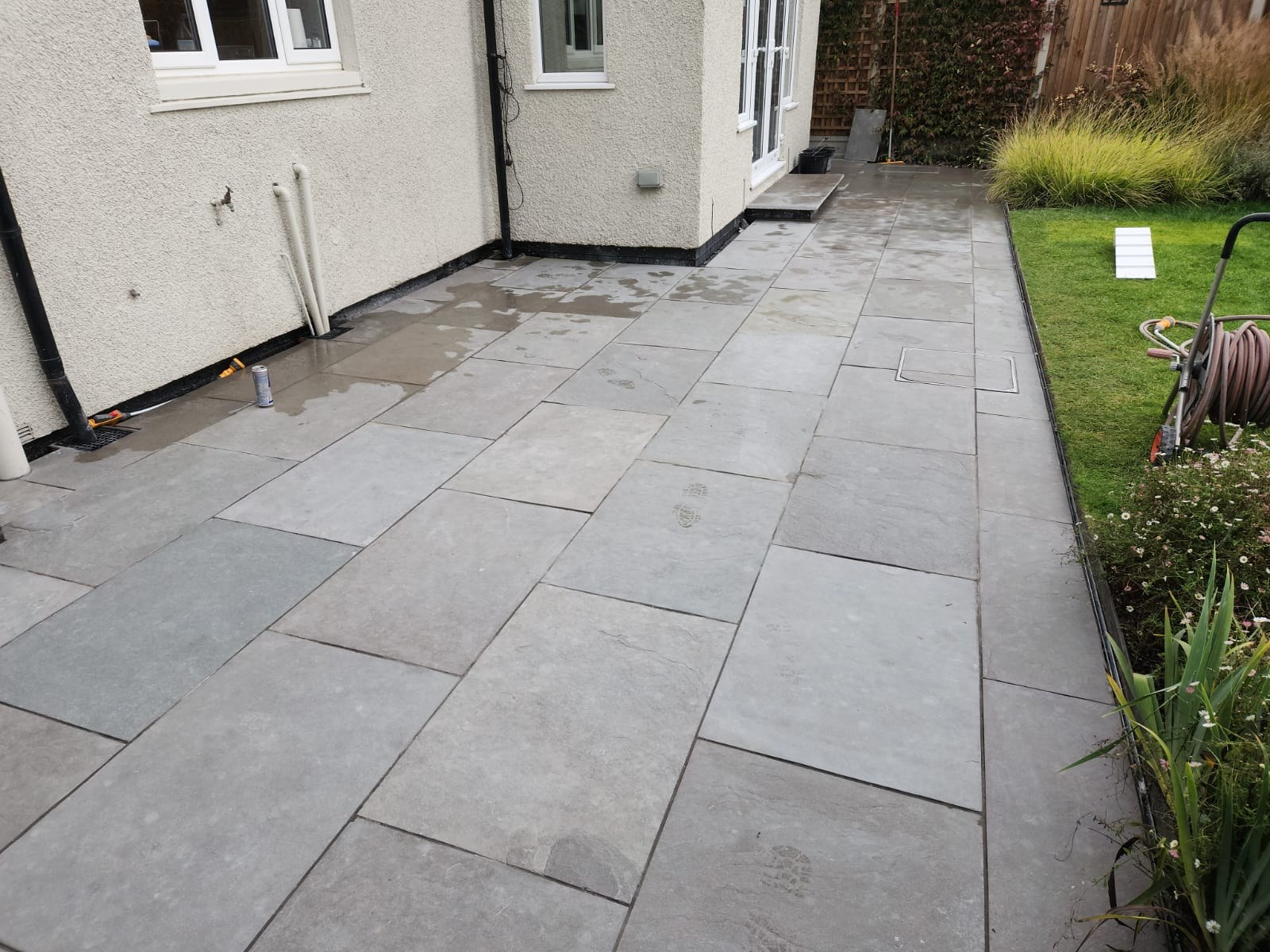 Finished grey sandstone patio laid against a rendered house wall on a completed Colchester patio installation