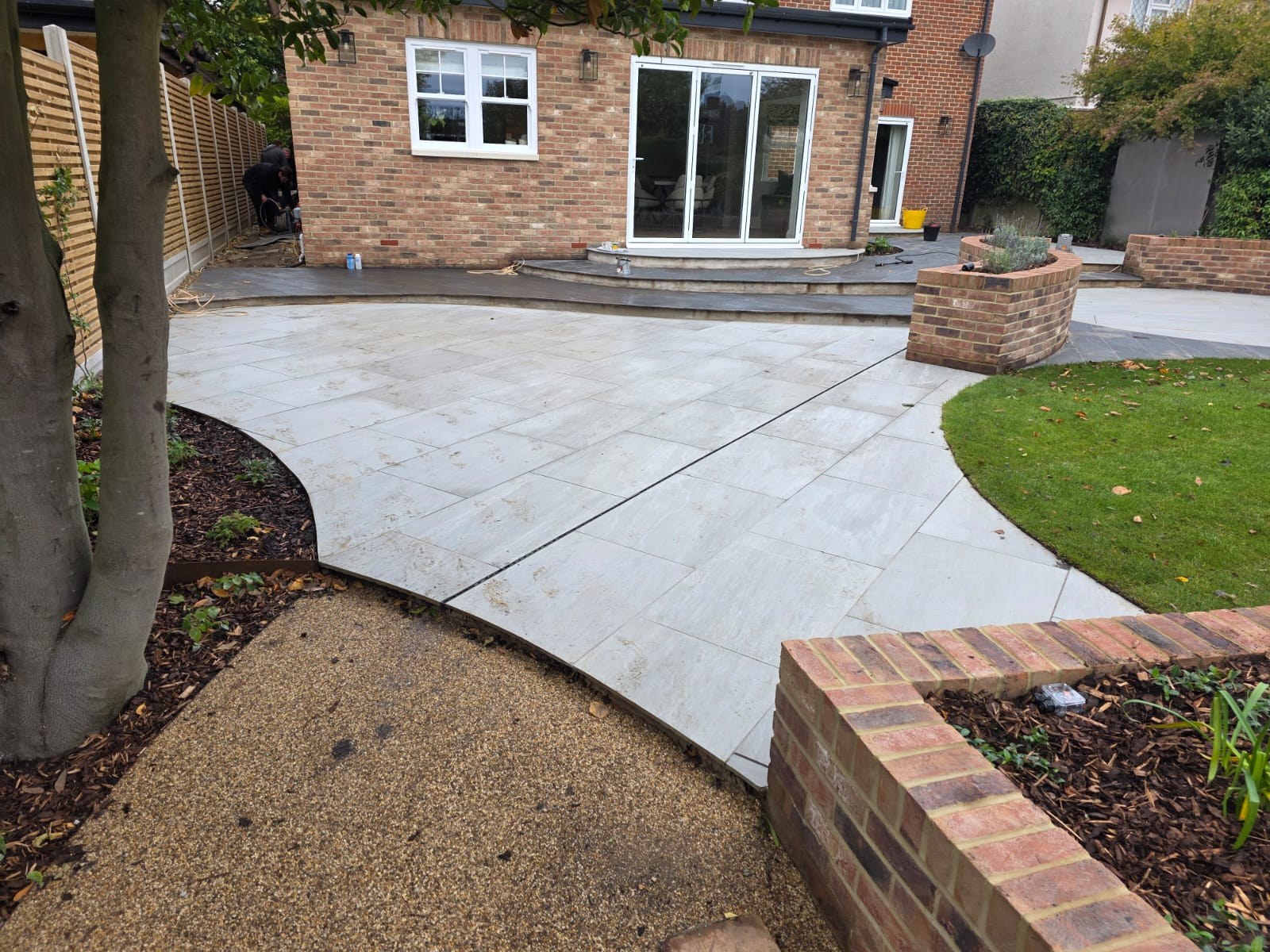 Light stone patio with curved brick planter walls at the rear of a house