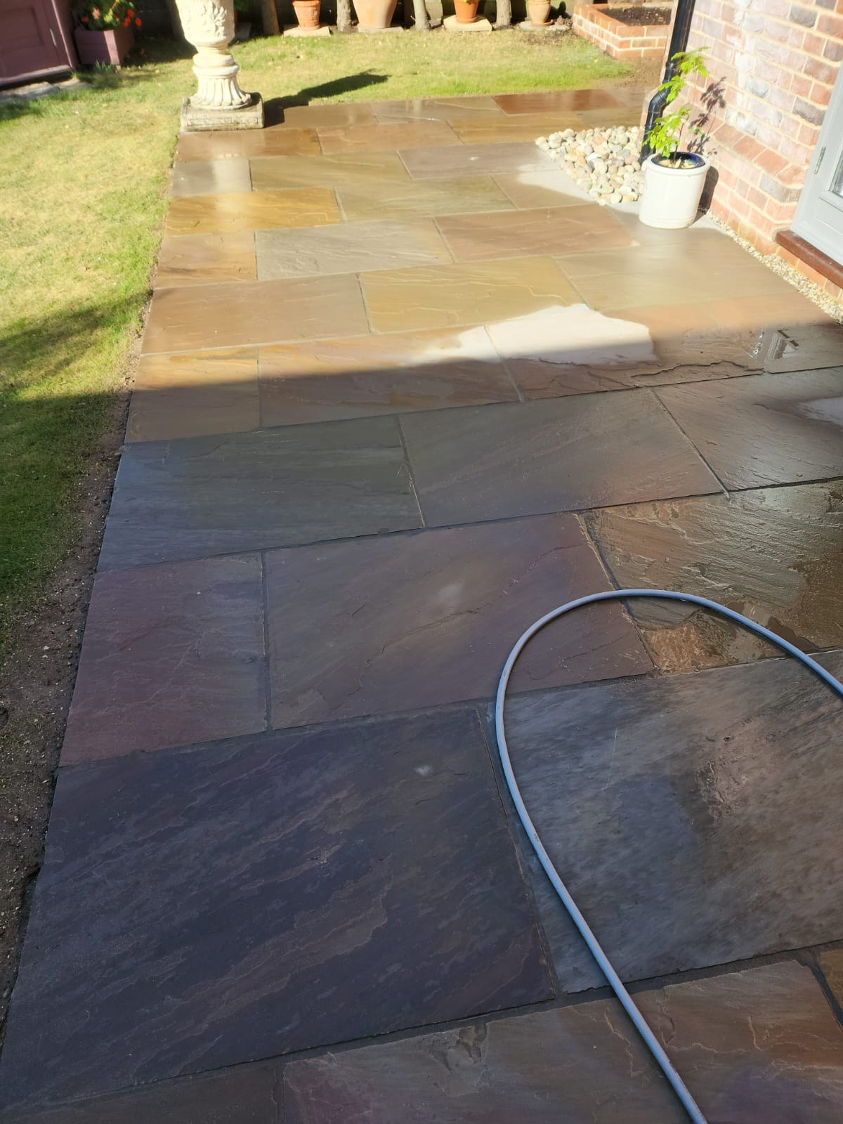 Multicoloured Indian sandstone patio path running alongside a lawn after jet washing