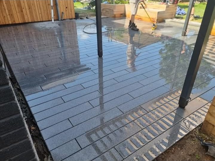 Grey wood-effect porcelain patio tiles being rinsed clean under a garden gazebo