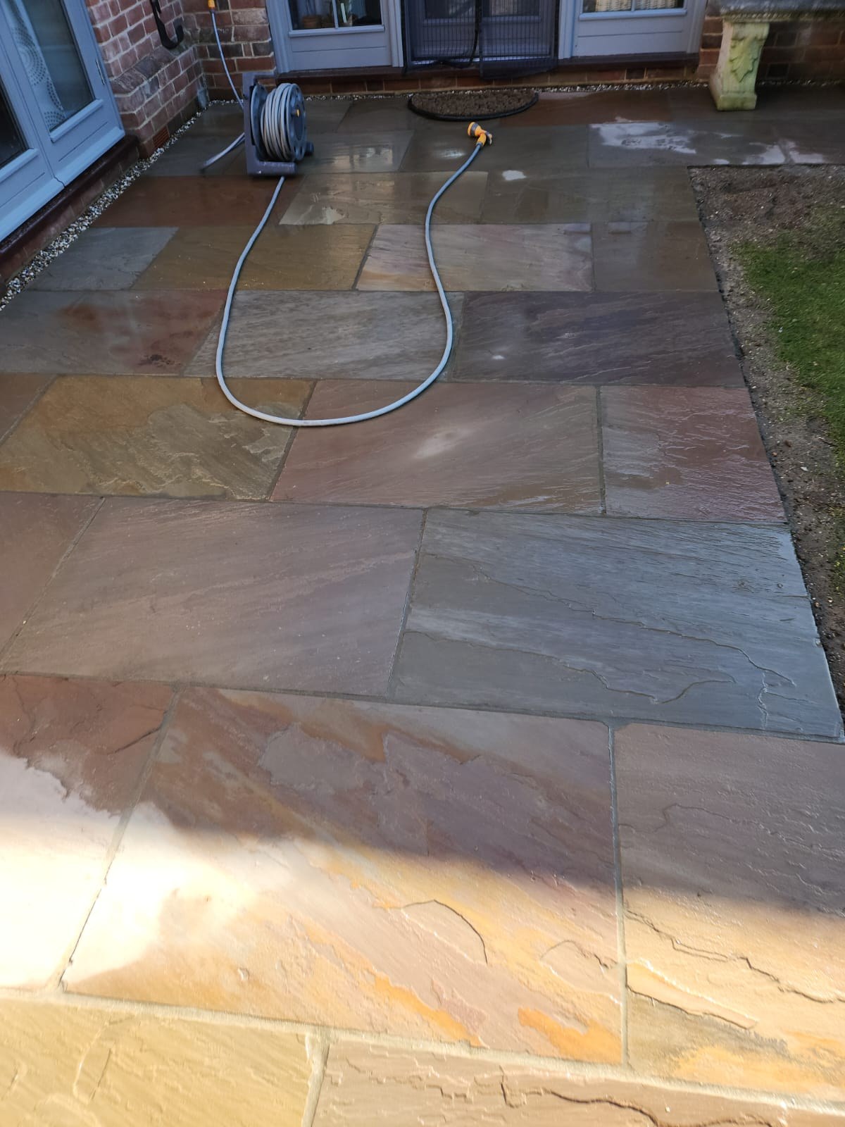 Multicoloured sandstone patio being washed down after pointing outside French doors
