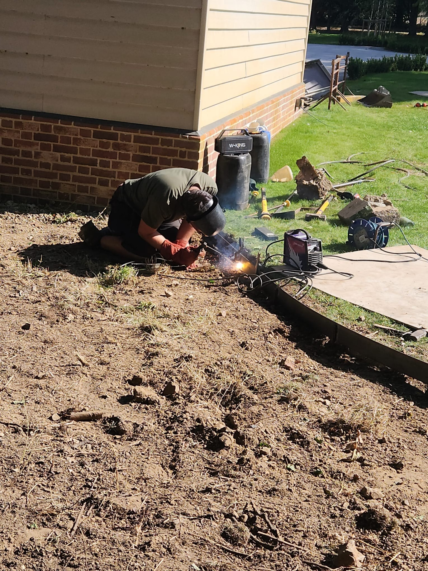 Ground cleared back to soil beside a house, with steel edging being welded in during groundworks