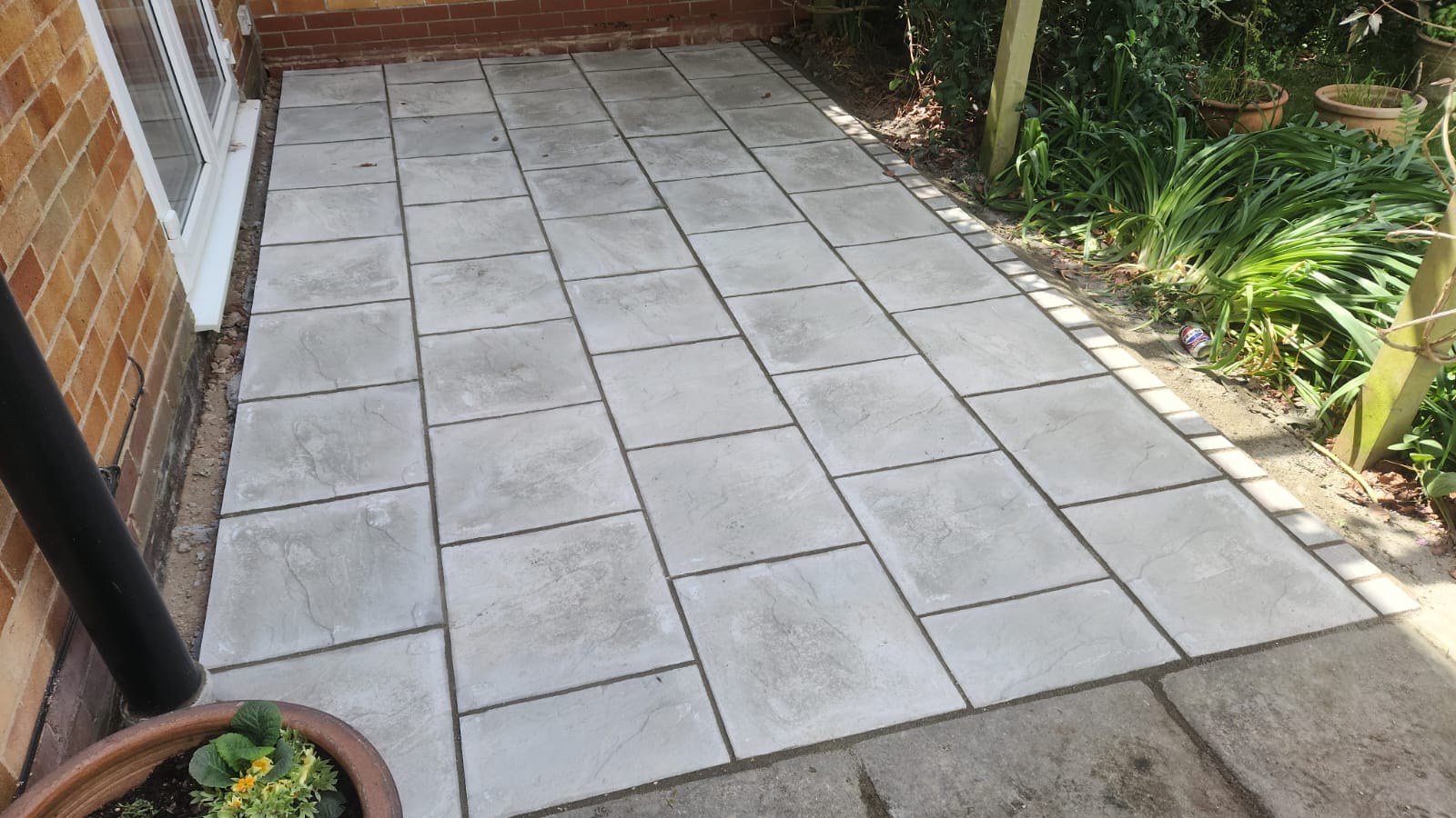 Small grey riven paving slab patio laid beside a brick house with block edging